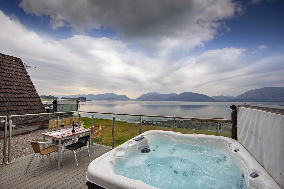 The hot tub and outdoor table on a lodge terrace looking down Loch Linnhe